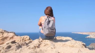 Sırt çantalı mutlu genç bir kadın bir kayanın üzerinde oturur ve aşağıdaki vadiye bakar. Karadeniz 'in kayalık sahillerindeki turistler. Özgürlük ve kolaylık kavramı