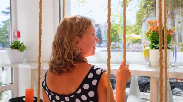 Woman goes for a drive on a swing near a cafe on a sunny day. The concept of freedom, making wishes and making dreams come true, sadness and thinking, back view : Sevastopol, Crimea - September 17 — Stock Video