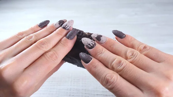Kobiece dłonie z pięknymi paznokciami manicure w postaci czekoladowych cukierków, łamiąc rozłożony batonik ciemnej czekolady, zbliżenie. Smacznego.. — Zdjęcie stockowe
