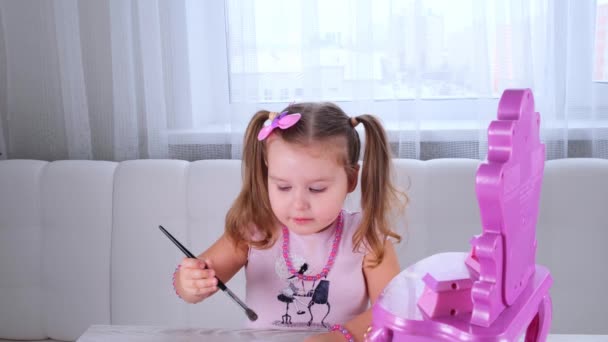 Linda niña de 3 años en vestido rosa y cuentas jugando con el maquillaje delante del espejo. — Vídeos de Stock