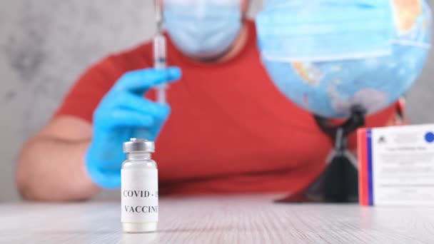 Vial con una vacuna contra el coronavirus, en el fondo un hombre está vacunando al planeta, el globo. Concepto de tratamiento del virus Corona, inyección durante una pandemia. Concepto de viaje durante una pandemia — Vídeos de Stock