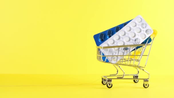 Winkelwagen met pillen op een gele achtergrond, close-up. Medicijnconcept, online winkelen — Stockvideo