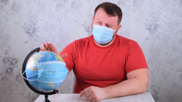 Man is sad about the illnesses on the plan and the lack of travel. male looks globe in protective mask and pandemic vaccine. Corona virus treatment concept, injection, clinical trials during a — Stock Video
