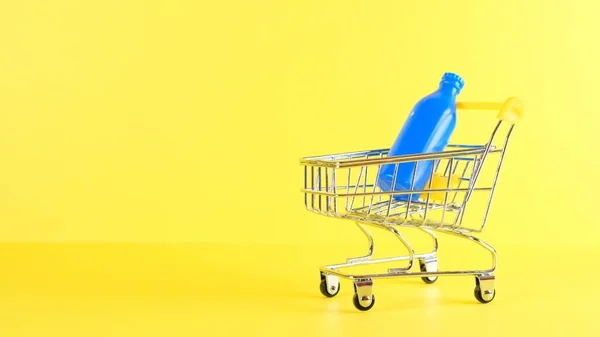 Carro de la compra con botellas en el interior sobre un fondo amarillo, primer plano. Viernes Negro Compras y descuento Concepto — Foto de Stock