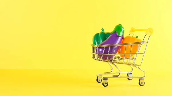 Carrito de compras con verduras en el interior sobre un fondo amarillo, primer plano. Viernes Negro Compras y descuento Concepto. — Foto de Stock
