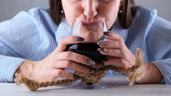 Vrouw grappige drankjes uit een wijnglas gebonden met een jute touw. Het concept van alcoholverslaving. Het probleem van alcoholisme — Stockfoto