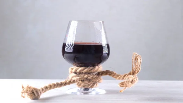 La copa de vino está atada con una cuerda. El concepto de dependencia del alcohol. — Foto de Stock