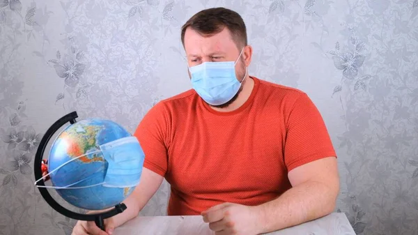 Maschio sta guardando il globo con una maschera protettiva e un vaccino pandemico. Concetto di trattamento del virus Corona, iniezione, studi clinici durante una pandemia. Concetto di viaggio durante una pandemia — Foto Stock