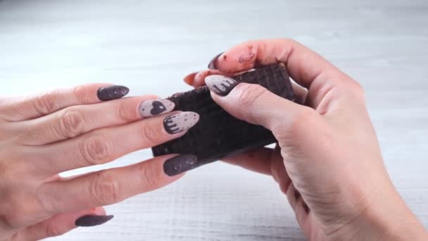 Жіноча рука з красивими манікюрними цвяхами у вигляді шоколадних цукерок, що тримає розгорнутий бар темного шоколаду, крупним планом. Насолоджуйтесь десертом . — стокове відео