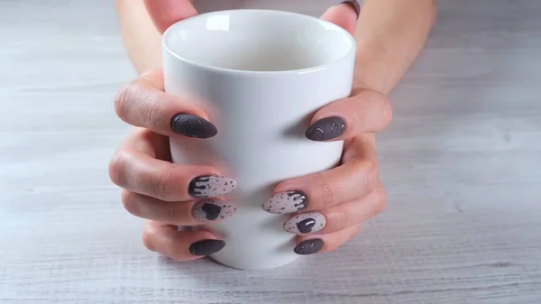 Piękne manicure paznokcie w postaci czekoladowych cukierków na kobiecych dłoniach zbliżenie i filiżankę kawy. — Zdjęcie stockowe
