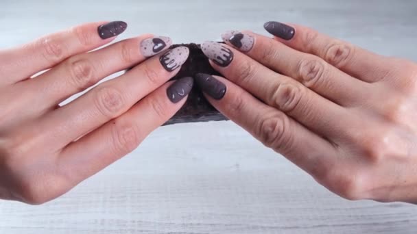 Vrouwelijke handen met prachtige manicure nagels in de vorm van chocolade snoepjes, het breken van een ontvouwde bar van pure chocolade, close-up. Geniet van het dessert. — Stockvideo