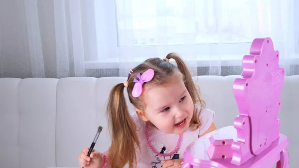 Mignonne petite fille de 3 ans en robe rose et perles jouant avec le maquillage devant le miroir. — Photo