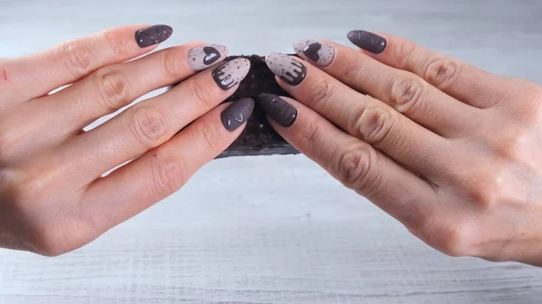 Weibliche Hand mit schönen Maniküre-Nägeln in Form von Schokoladenbonbons, die eine entrollte Tafel dunkler Schokolade in Nahaufnahme hält. Dessert genießen. — Stockfoto