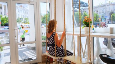 Kadın güneşli bir günde bir kafede salıncakta sallanıyor. Özgürlük kavramı, dilekleri gerçekleştirmek ve hayalleri gerçekleştirmek, üzüntü ve düşünce, geriye bakış: Sivastopol, Kırım - 17 Eylül