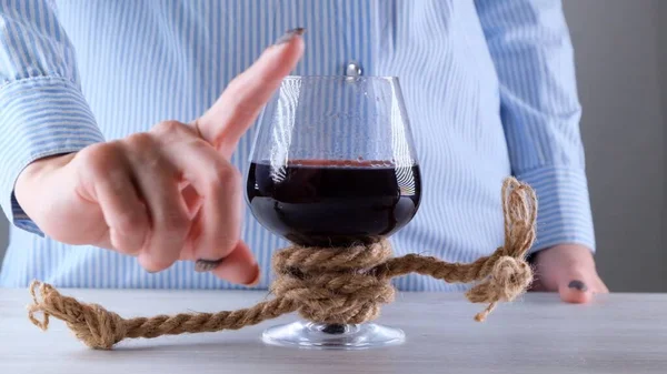 Mão feminina mostra o sinal CANNOT, PARAR em um copo de vinho, amarrado com uma corda de juta. O conceito de dependência de álcool. O problema do tratamento do alcoolismo — Fotografia de Stock