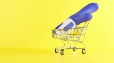 Shopping cart and dildo a yellow background, closeup. Black Friday Shopping and Discount Concept. Intimate shopping.