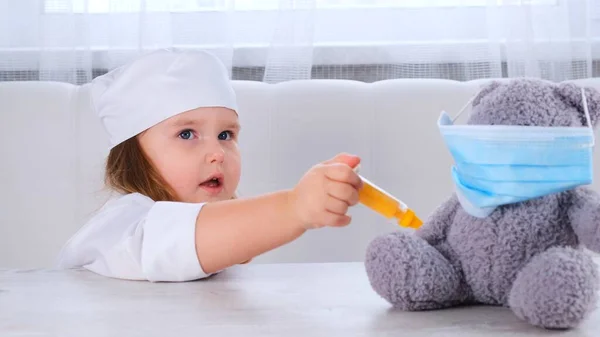 Little girl plays a doctor, makes an injection. Happy child little doctor examines a teddy bear. Corona virus treatment concept, injection during pandemic — Stock Photo, Image