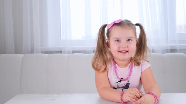 Portret ślicznej uśmiechniętej dziewczyny w wieku 3-4 lat z dużymi oczami i piękną fryzurą z różowym kokardką, śmiejącym się dzieckiem, koralikami i innymi dekoracjami. — Wideo stockowe