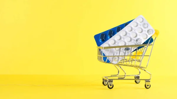 Carro de la compra con pastillas sobre fondo amarillo, primer plano. Concepto de medicina, compras online — Foto de Stock