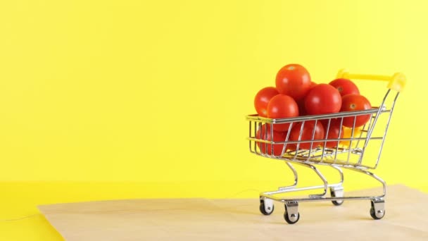 Einkaufswagen mit Kirschtomaten drinnen auf gelbem Hintergrund, Nahaufnahme. Black Friday Shopping und Discount-Konzept — Stockvideo
