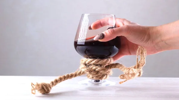 Mano femenina sosteniendo copa de vino está atado con una cuerda de yute. El concepto de dependencia del alcohol. — Foto de Stock