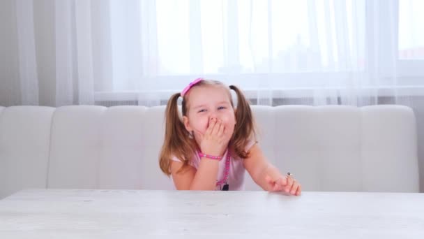 Retrato de uma menina sorridente bonito 3-4 anos com olhos grandes e um belo penteado com um arco-de-rosa, rindo criança, contas e outras decorações. — Vídeo de Stock