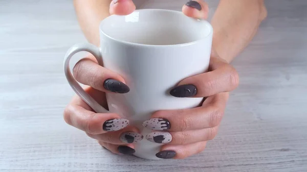 Piękne manicure paznokcie w postaci czekoladowych cukierków na kobiecych dłoniach zbliżenie i filiżankę kawy. — Zdjęcie stockowe
