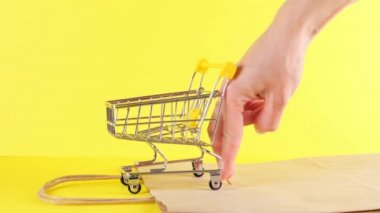 Kadın eli, sarı arka planda oyuncak bir alışveriş arabasını itiyor. Kara Cuma Alışveriş ve İndirim Konsepti
