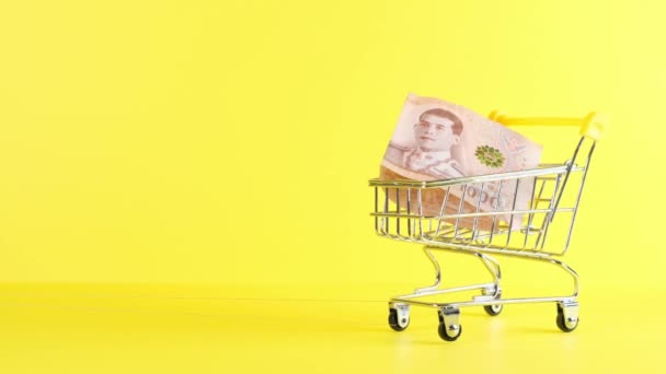 Carrello della spesa e mille baht tailandesi su sfondo giallo, primo piano. Venerdì nero Shopping e Sconto Concetto — Video Stock