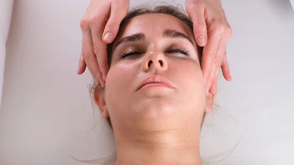 Massaggio viso trattamento di bellezza. Primo piano di una giovane donna faccia sdraiata sulla schiena, ottenere massaggio lifting facciale, pizzicare e rotolare tecnica — Foto Stock