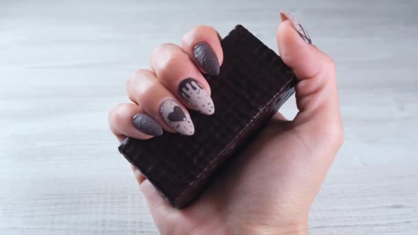 Женская рука с красивыми маникюрными ногтями в виде шоколадных конфет, с развернутой полосой тёмного шоколада крупным планом. Насладитесь десертом. — стоковое видео