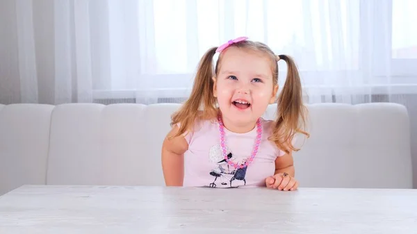 Portrait d'une jolie jolie fille rieuse de 3-4 ans avec de gros yeux et une belle coiffure avec un arc rose, enfant riant, perles et autres décorations. — Photo