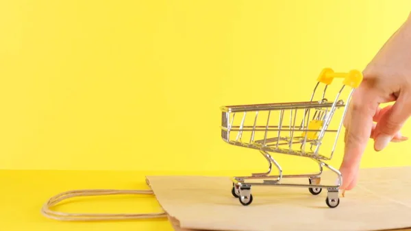 Mano femenina empuja un juguete carrito de compras sobre un fondo amarillo, primer plano. Viernes Negro Compras y descuento Concepto — Foto de Stock