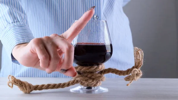 Женская рука показывает знак НЕ МОЖЕТ, ОСТАНОВИТЬ на бокале вина, привязанный джутовой веревкой. Концепция алкогольной зависимости. Проблема лечения алкоголизма — стоковое фото