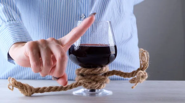 Female hand shows the sign CANNOT, STOP on a wine glass, tied with a jute rope. The concept of alcohol addiction. The problem of alcoholism treatment — Stock Photo, Image