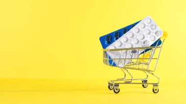Sarı arka planda hapları olan alışveriş arabası, yakın plan. Tıp konsepti, online alışveriş