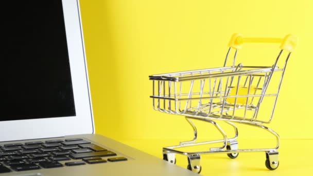 Shopping basket next to a laptop on a yellow background. Copy space. Online shopping concept. — Stock Video