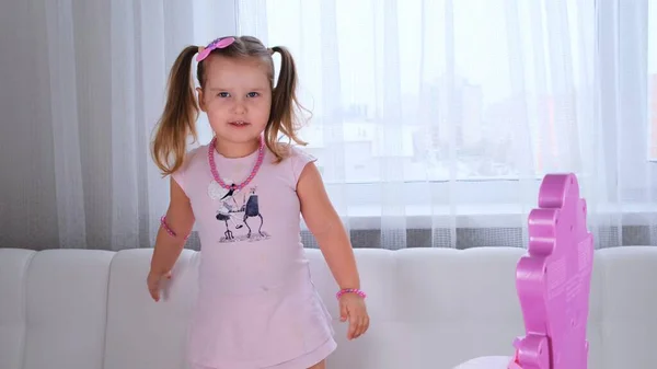 Niedliche kleine 3-jährige Mädchen in rosa Kleid und Perlen spielen mit Make-up vor dem Spiegel. — Stockfoto
