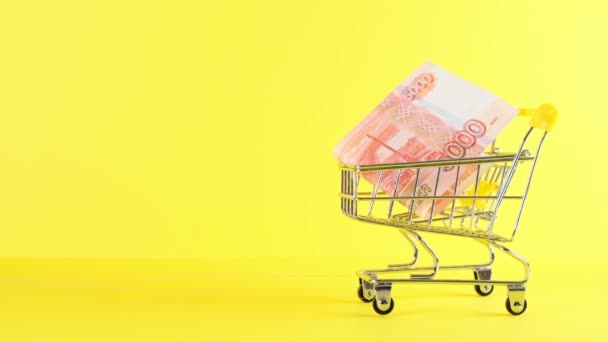 Shopping cart with a bill of five thousand Russian rubles on a yellow background, closeup. Black Friday Shopping and Discount Concept — Stock Video