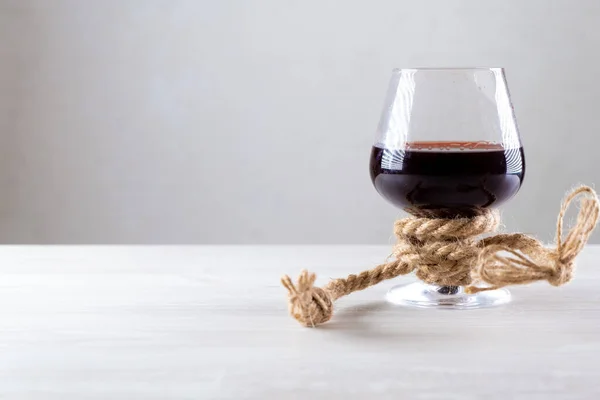 Copa de vino tinto está atado con una cuerda. El concepto de adicción al alcohol. espacio de copia. — Foto de Stock