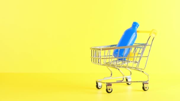 Carro de la compra con botellas en el interior sobre un fondo amarillo, primer plano. Viernes Negro Compras y descuento Concepto — Vídeos de Stock