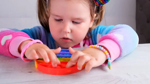 Portrait blonde girls with pop it sensory toy hand form. little female presses colorful rainbow squishy soft silicone bubbles on white background. Stress and anxiety relief. Trendy fidgeting game. — Stock Photo, Image