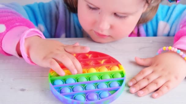 Söta små flickor leker med entusiasm pop det sensoriska leksak cirkel form. små kvinnliga pressar färgglada regnbåge squishy mjuka silikonbubblor på vit bakgrund. Stress och ångestlindring. Trendig — Stockvideo