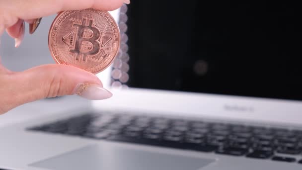 Kvinnlig hand håller Golden bitcoin med anteckningsbok. Suddig av en bärbar dator och Cyrptocurrency Bitcoin Computer. business of money digitalt koncept. — Stockvideo