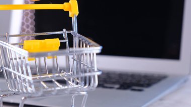 Arka planda dizüstü bilgisayarın yanında alışveriş sepeti var. Uzayı kopyala Çevrimiçi alışveriş kavramı.