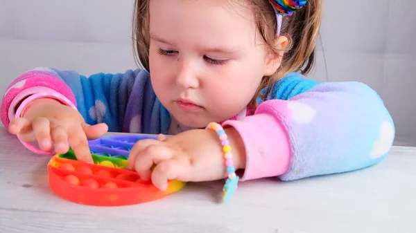 Cute little girls with pop it sensory toy. little female presses colorful rainbow squishy soft silicone bubbles on white background. Stress and anxiety relief. Trendy fidgeting game. — Stock Photo, Image