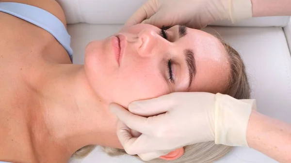 Massaggio viso trattamento di bellezza. Primo piano di una giovane donna faccia sdraiata sulla schiena, ottenere massaggio lifting facciale, pizzicare e rotolare tecnica — Foto Stock