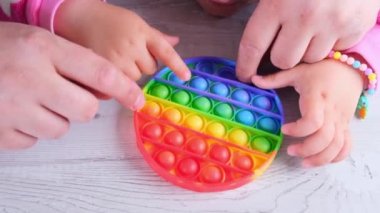 Şirin küçük kızlar babalarıyla oynuyorlar. Duyusal oyuncak çemberi formunda. Küçük dişi, beyaz arka planda renkli gökkuşağı yumuşak silikon kabarcıklar oluşturur. Stres ve endişe giderici. Eğilim