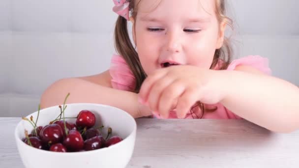 Mooi glimlachend klein schattig meisje zitten met een bord kersen en het eten van een bes — Stockvideo