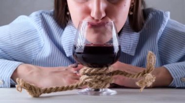 Kadın komedisi, jüt halatla bağlanmış bir şarap kadehinden içer. Alkol bağımlılığı kavramı. Alkolizm tedavisi sorunu